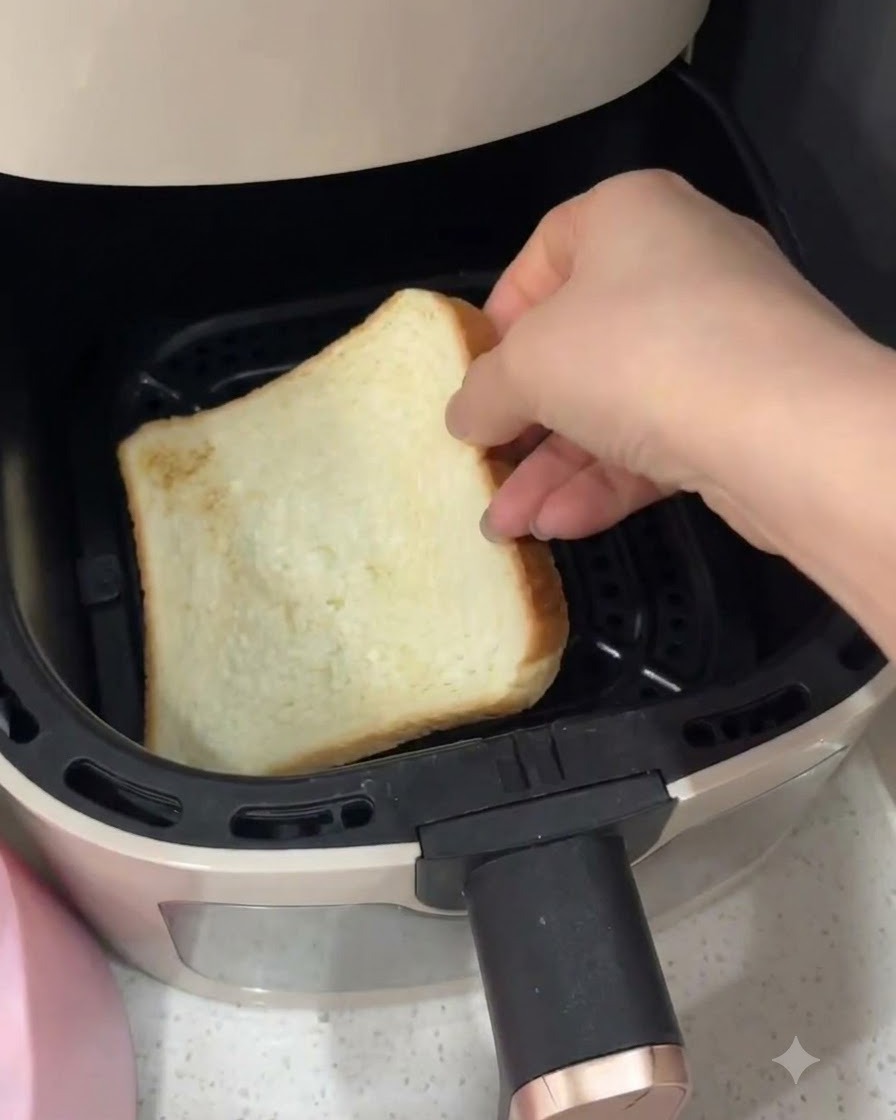에어프라이어 바구니 안에 하얀 식빵 한 조각을 손으로 넣는 모습