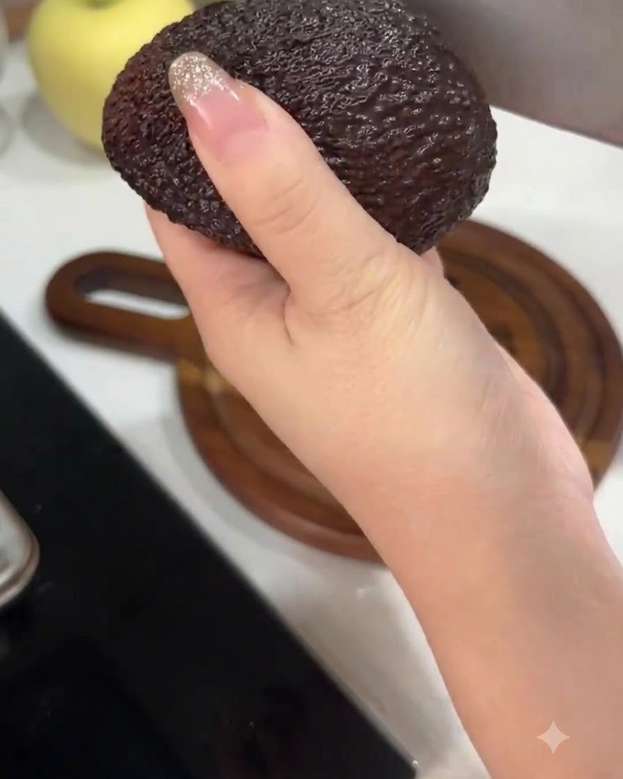 큰 주방용 칼로 아보카도를 반으로 자르며 손으로 잡고 있는 모습