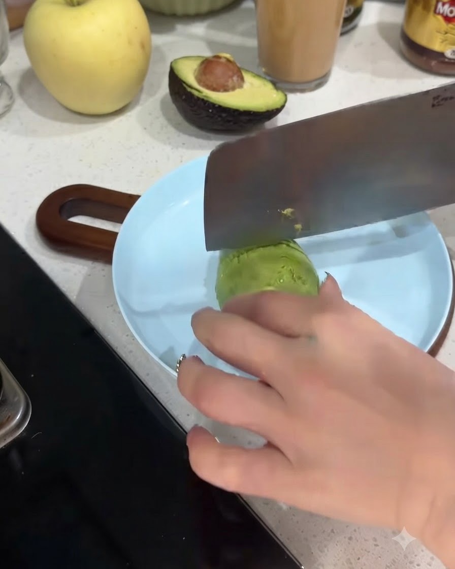 하늘색 접시 위에서 껍질 벗긴 아보카도 반쪽을 얇은 조각으로 썰고 있는 모습
