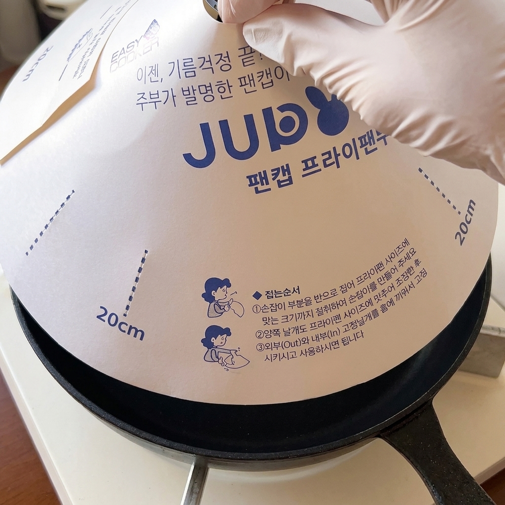 치즈가 얹어진 햄버거 패티가 담긴 프라이팬 위에 하얀 종이 뚜껑이 덮이는 모습.