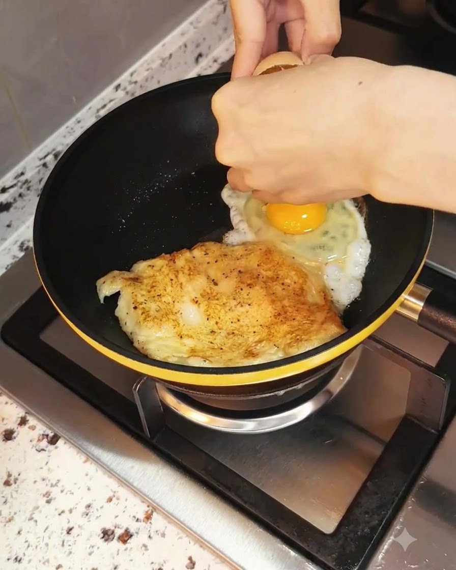 조리 중인 닭가슴살 옆 프라이팬에 달걀을 깨서 넣는 모습.