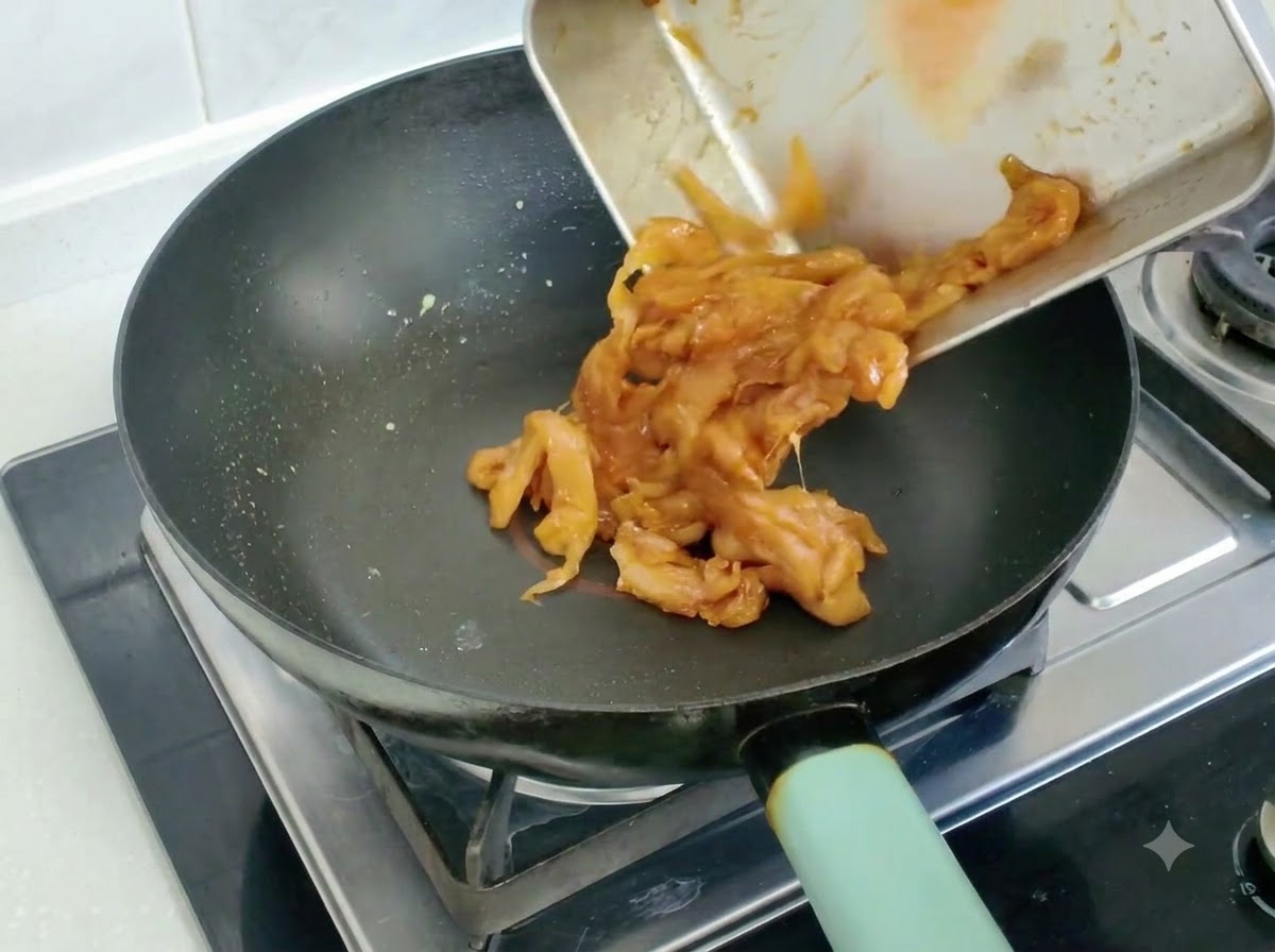 프라이팬에 쏟아져 볶아지고 있는 마리네이드된 닭고기 조각들.