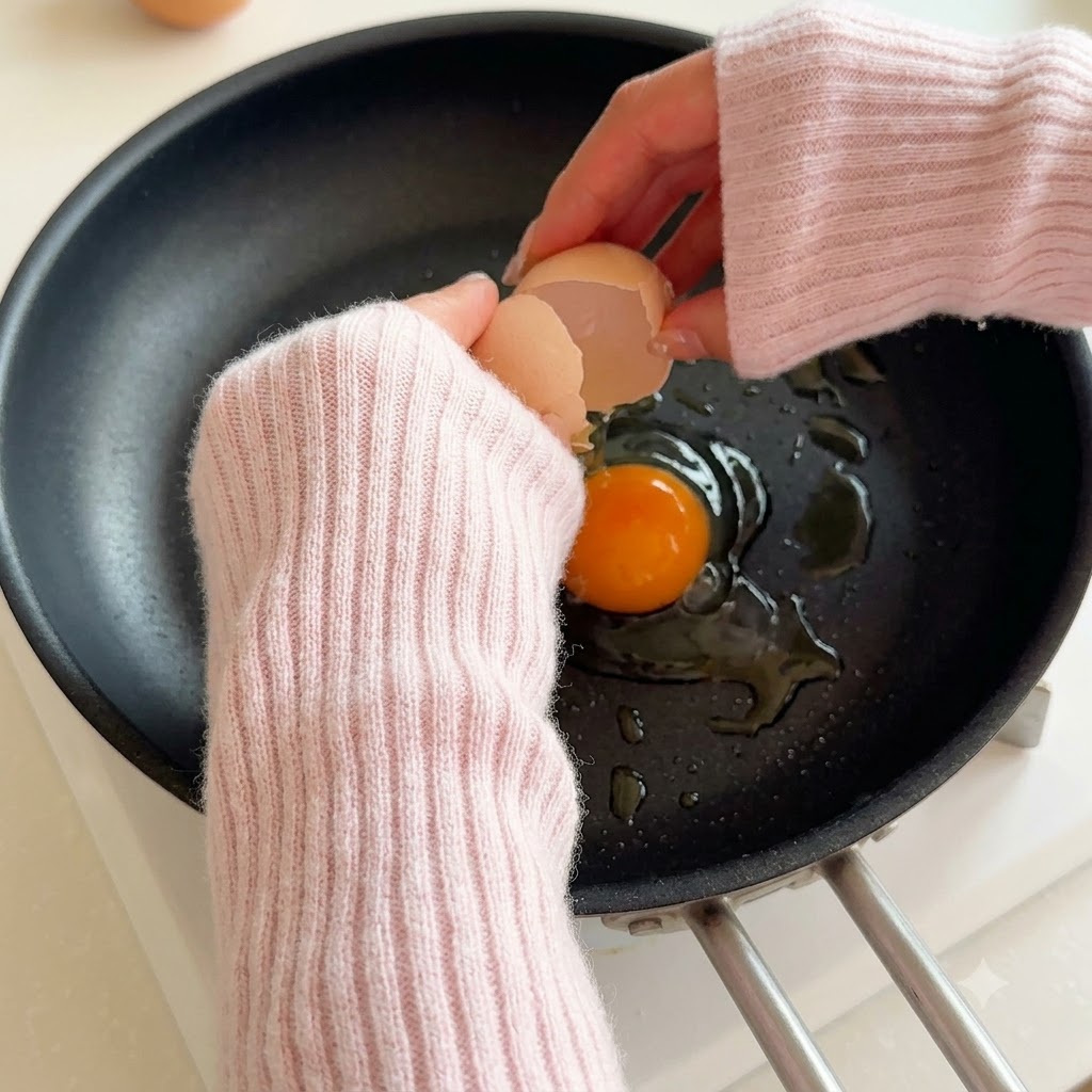 기름을 두른 뜨거운 팬 위로 달걀이 깨어져 들어가는 모습.