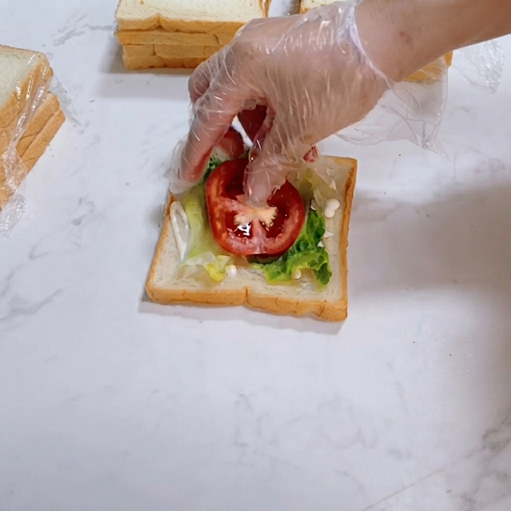 신선한 붉은 토마토 슬라이스가 빵 조각 위의 양상추 위에 조심스럽게 놓여지는 모습.