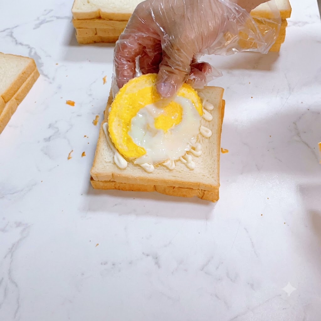 마요네즈를 바른 흰 식빵 위에 달걀프라이가 조심스럽게 놓여지는 모습.