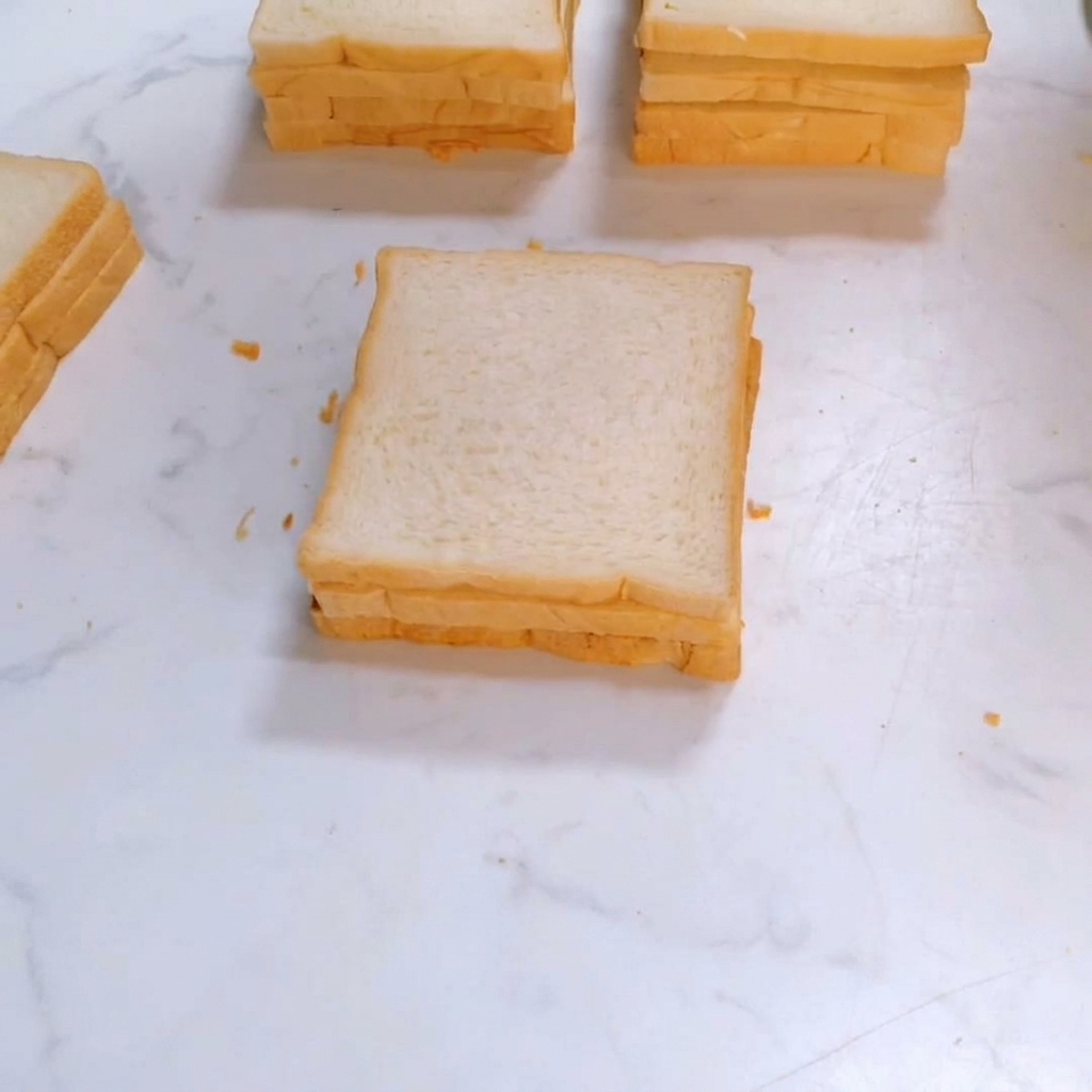 네모난 흰 식빵의 세 번째 조각이 샌드위치 더미 위에 올려지는 모습.