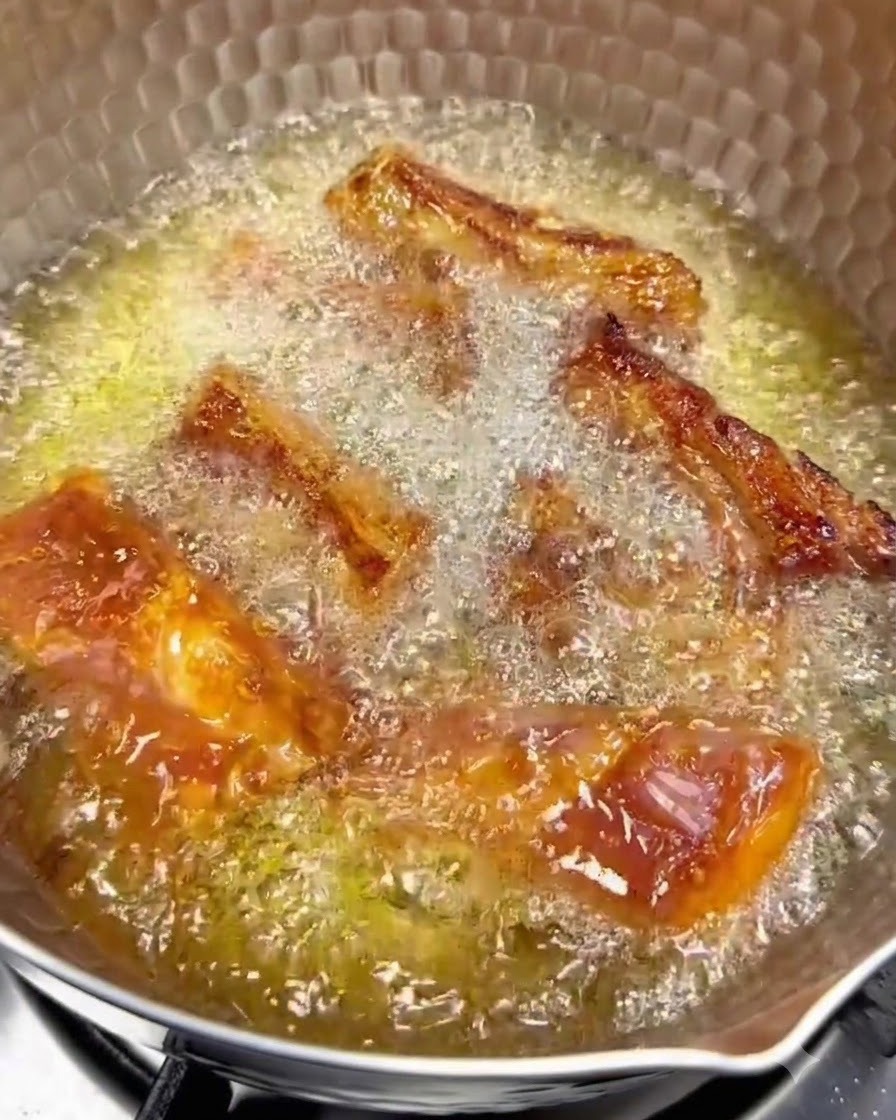약불에서 뜨거운 기름에 튀겨지며 표면이 노릇하게 변하는 돼지갈비의 모습.