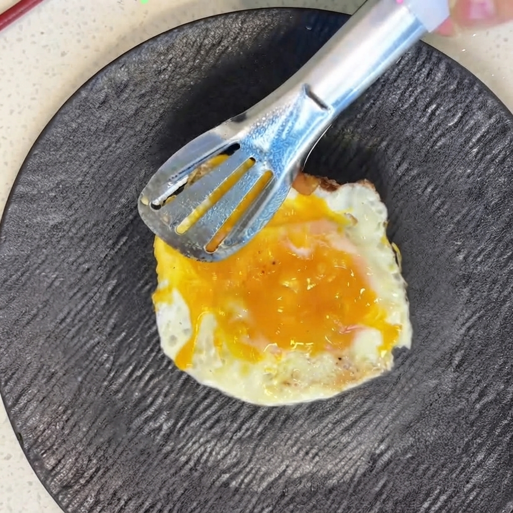 금속 집게를 사용하여 썬 토마토 위에 갓 구운 달걀 후라이를 조심스럽게 올리는 모습.