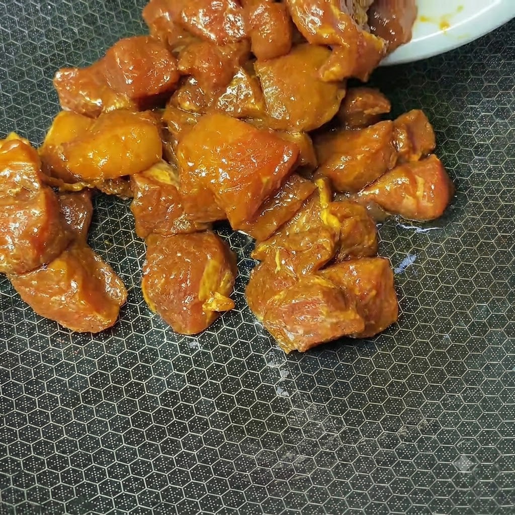 달궈진 텍스처가 있는 웍에서 조리 중인 불그스름한 양념 돼지고기 큐브.
