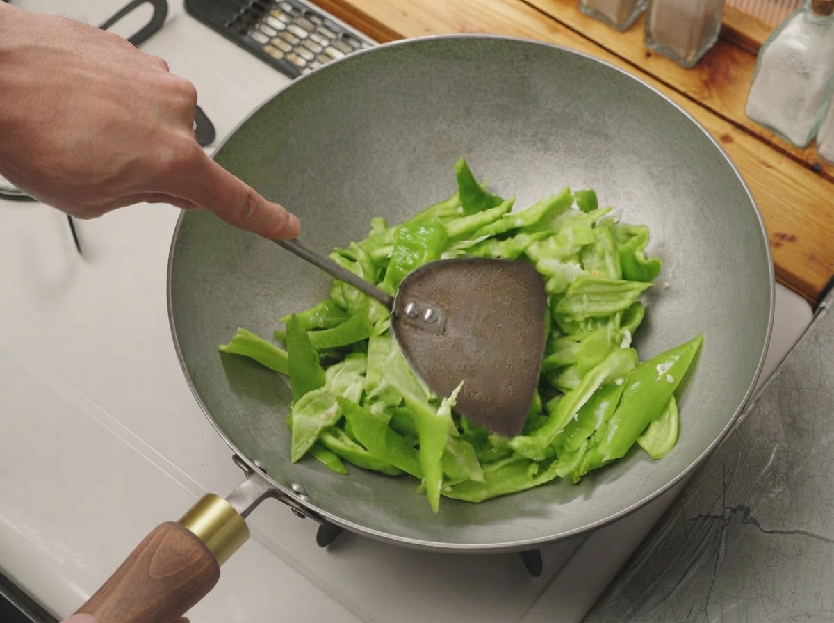 달궈진 마른 웍 안에서 금속 뒤집개로 썰어둔 고추를 볶고 있는 모습.