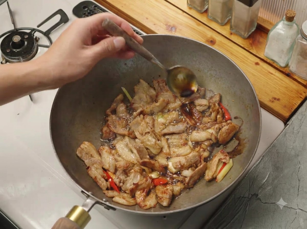 고기와 향신채가 담긴 뜨거운 웍 테두리를 따라 숟가락으로 간장을 붓고 있는 모습.