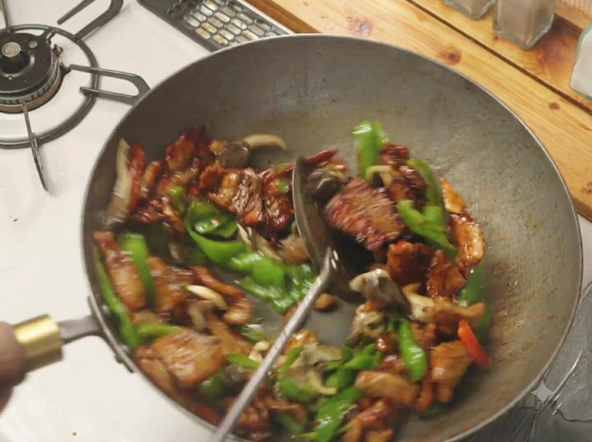 뜨거운 웍 안에서 뒤집개로 고추, 버섯, 삼겹살을 골고루 섞어 볶는 모습.