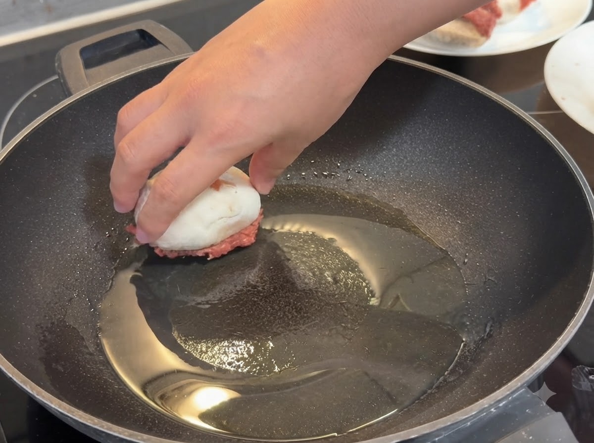 기름이 둘러진 뜨거운 프라이팬에 속을 채운 버섯을 고기 면이 아래로 가도록 손으로 올리는 모습.
