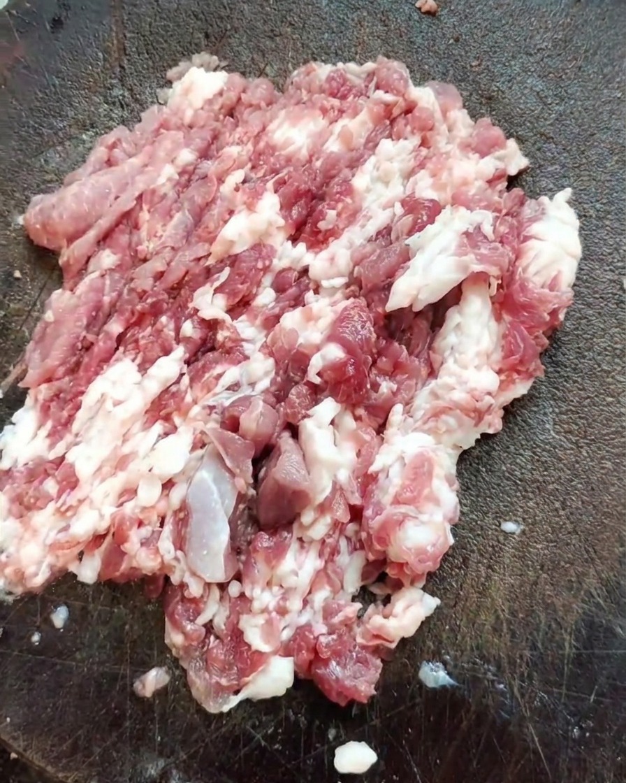 질감이 살아있는 나무 도마 위에 갓 다진 돼지고기 덩어리와 날카로운 중식도가 놓여 있습니다.