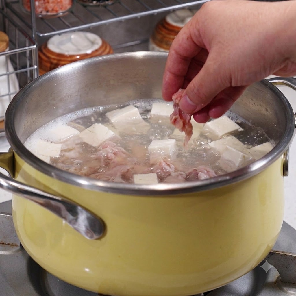 끓고 있는 육수, 두부, 해산물이 담긴 냄비에 재운 돼지고기를 손으로 넣는 모습.