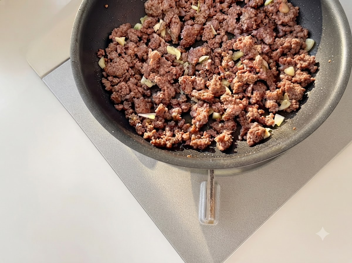 프라이팬에서 노릇하게 볶아진 다진 소고기와 다진 마늘, 톳토마토를 함께 볶는 모습.