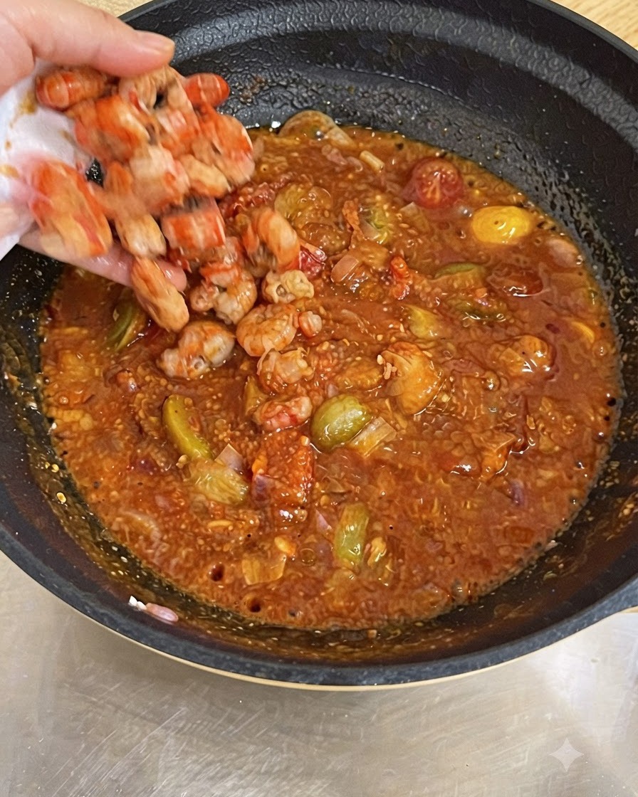 보글보글 끓는 붉은 토마토 소스 팬에 익힌 새우를 넣는 손.