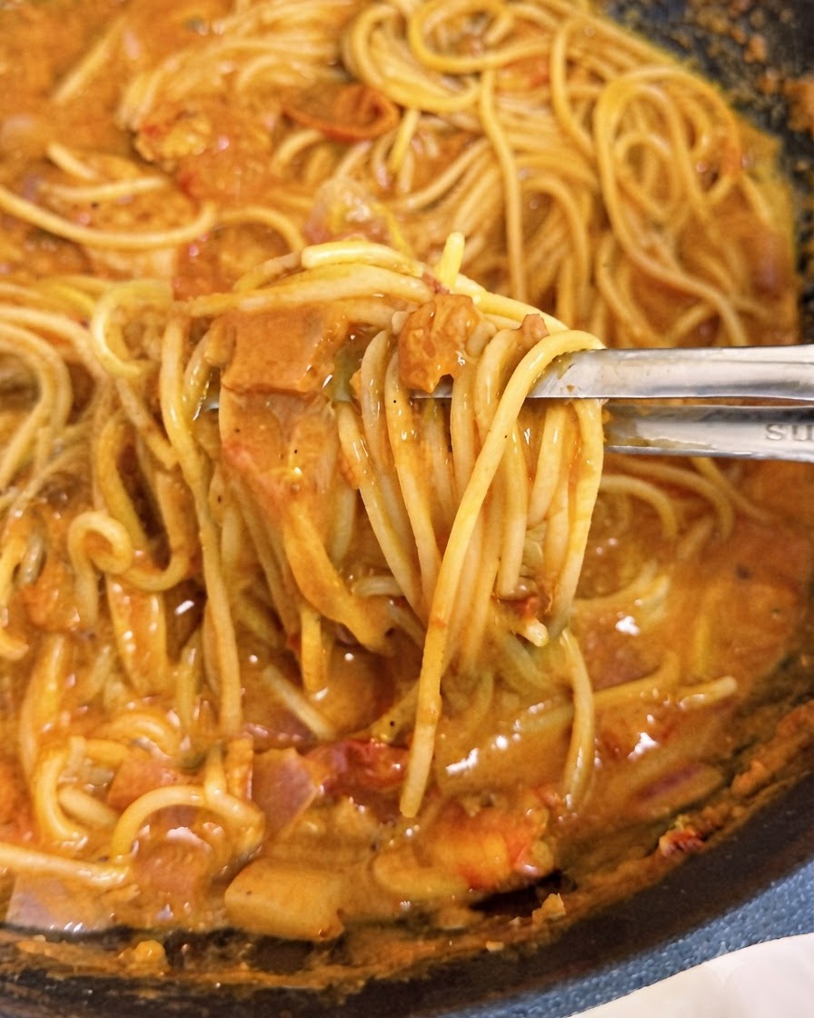 웍 안에서 집게로 크리미한 분홍빛 토마토 소스가 코팅된 스파게티 면발을 들어 올리는 모습.