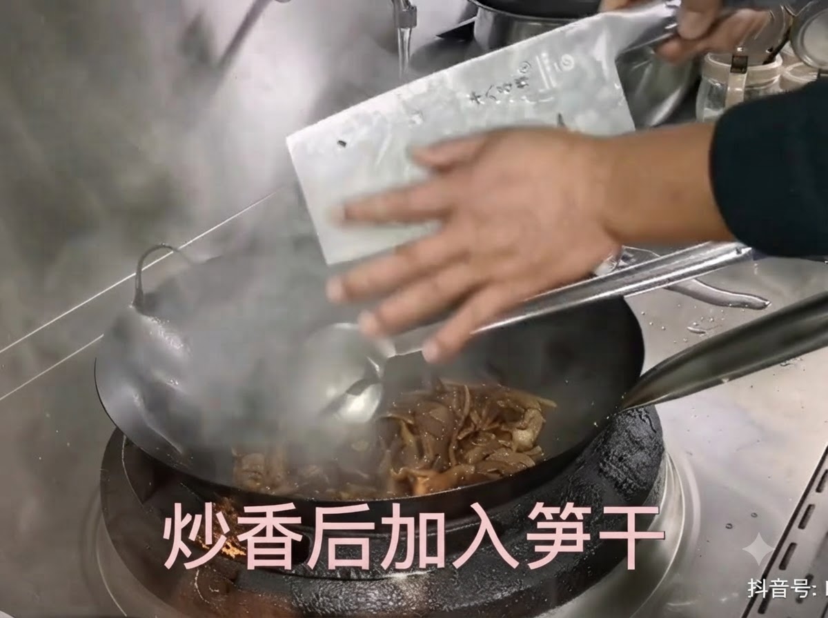 칼끝으로 불린 말린 죽순을 긁어내어 고기가 볶아지고 있는 뜨거운 웍에 넣는 모습.