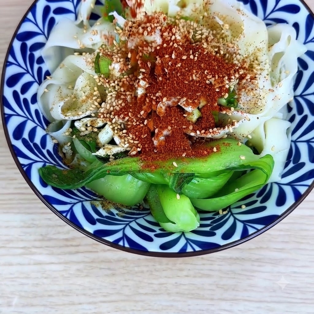 그릇 안의 국수와 양념 위에 고운 고추가루와 굵은 고추가루를 고르게 뿌린 모습.