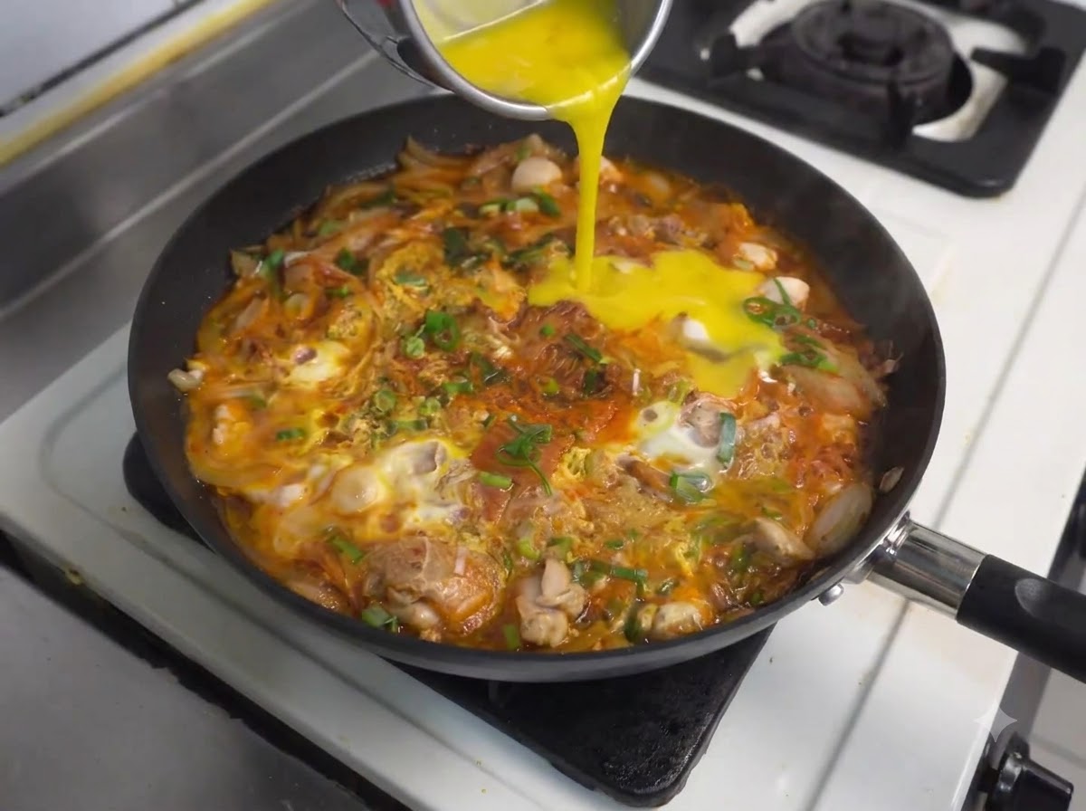 닭고기와 김치가 끓고 있는 팬에 용기에서 추가 달걀물이 부어지는 모습.