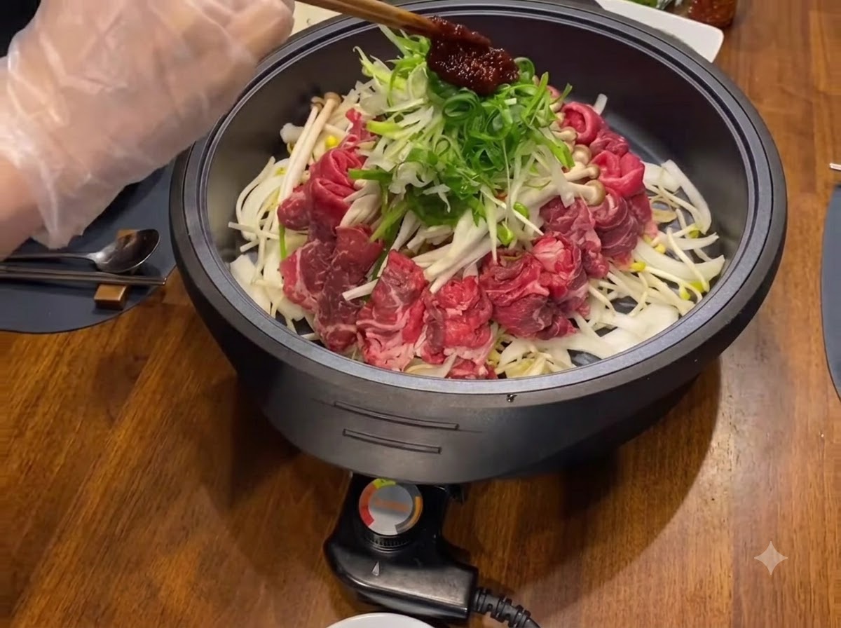 검은색 조리 팬 안의 채 썬 쪽파와 고기 위에 붉은색 양념장 한 스쿱이 얹혀 있습니다.