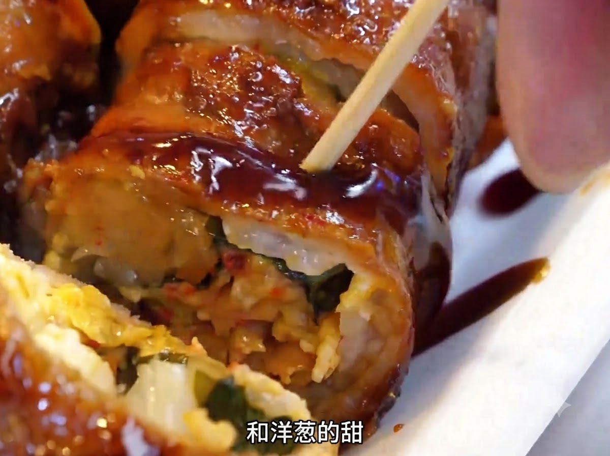 금속 뒤집개를 사용하여 뜨거운 철판 위의 고기말이를 뒤집는 모습.