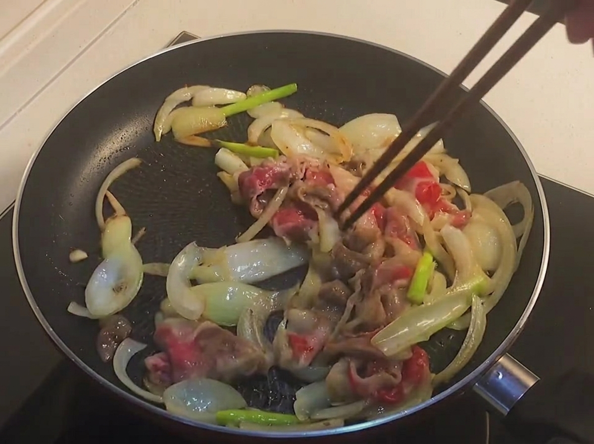 프라이팬에서 겉면이 살짝 익은 우삼겹과 양파를 젓가락으로 섞는 모습.