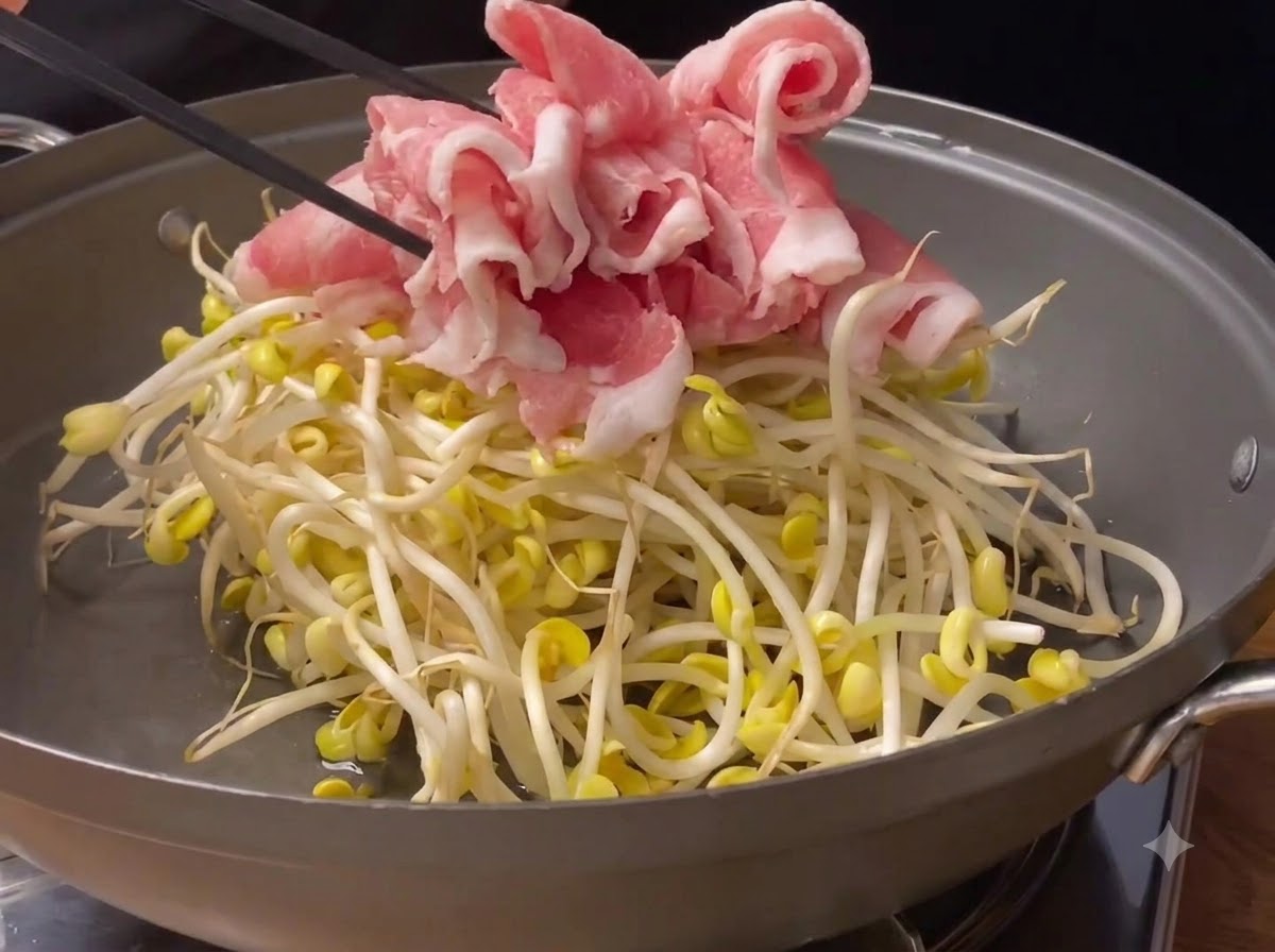 팬 안의 콩나물 위에 얇게 썰린 돼지고기를 올리는 모습.