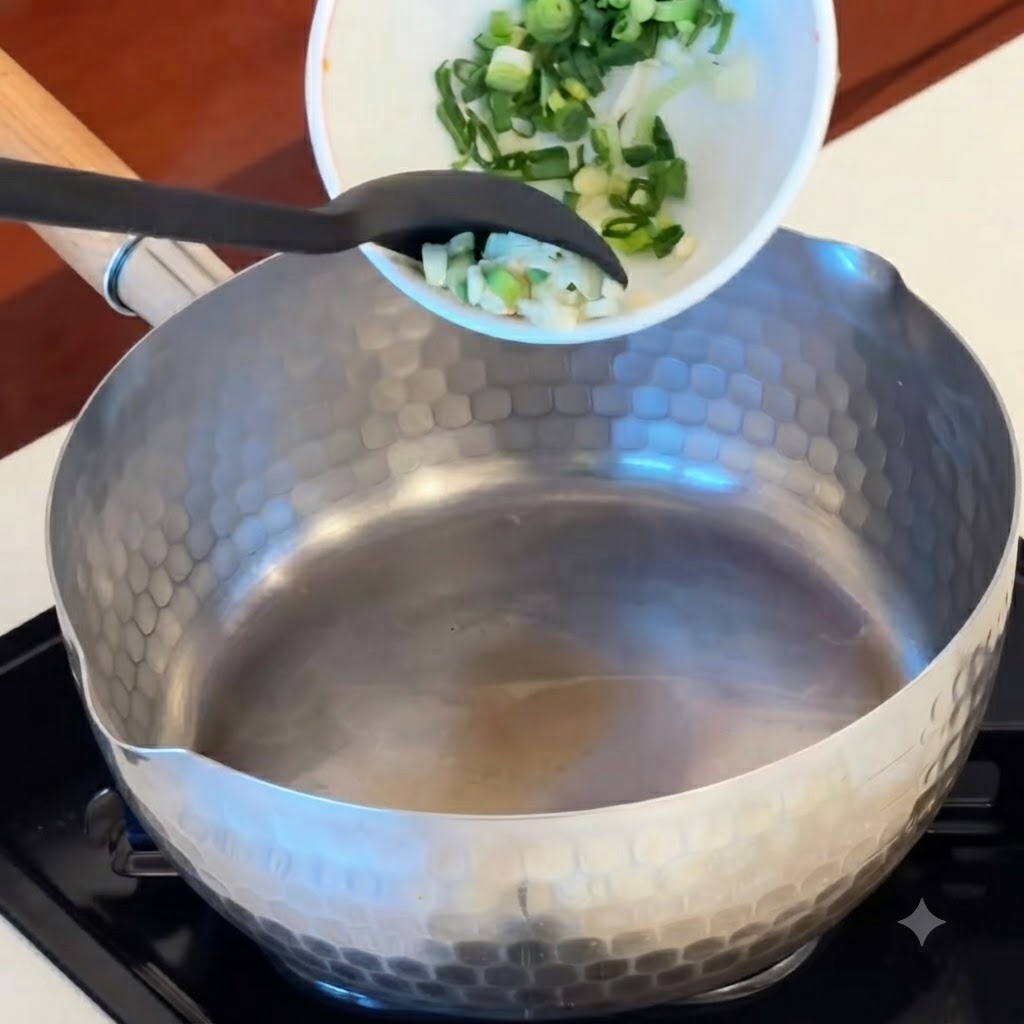 볼에 담겨 있던 편 마늘, 붉은 김치 조각, 소시지 동그라미들이 달궈진 냄비로 쏟아지는 모습.