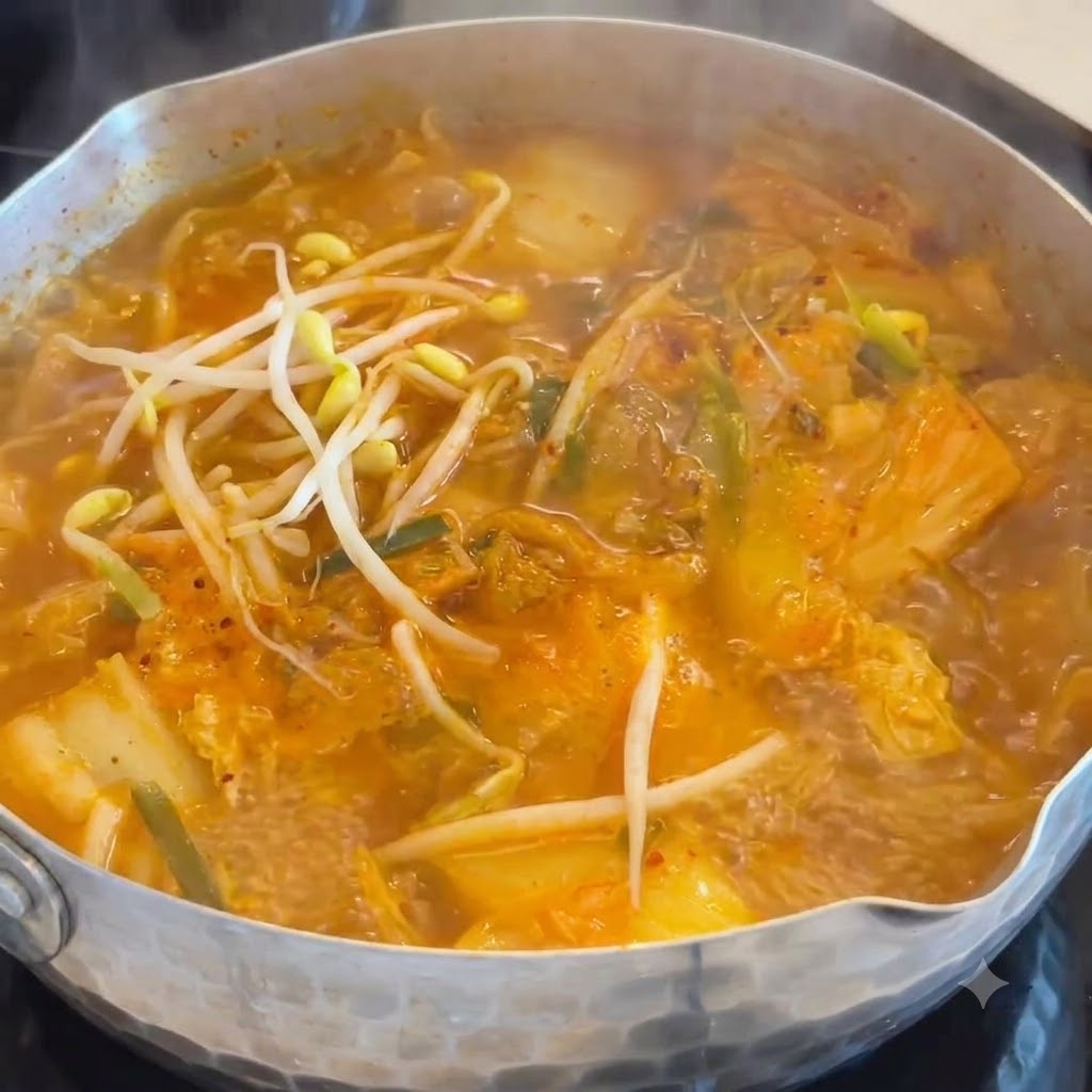 주황색 김치 소시지 국물이 끓는 냄비 속으로 아삭한 하얀 콩나물이 투입되는 모습.