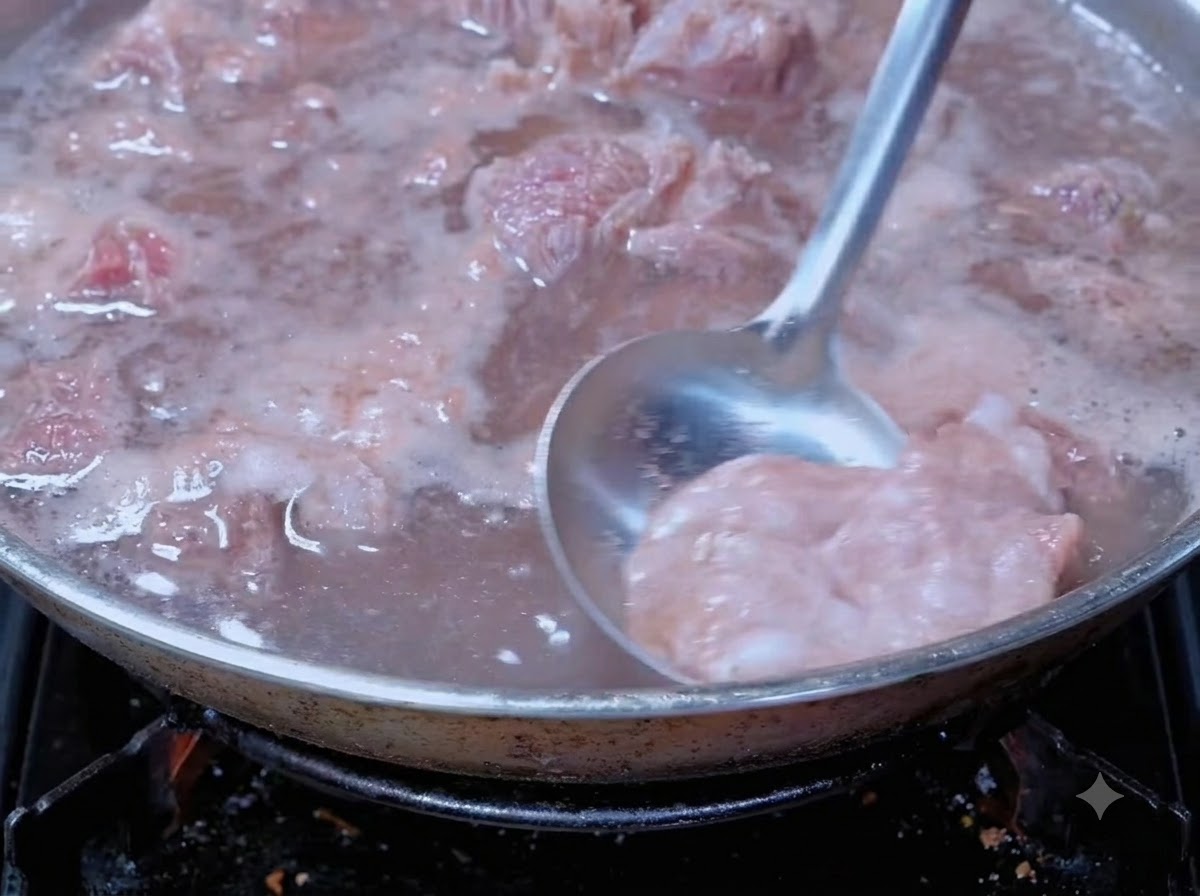 요리용 냄비에서 끓는 소고기의 핏물 거품을 국자로 걷어내는 모습.