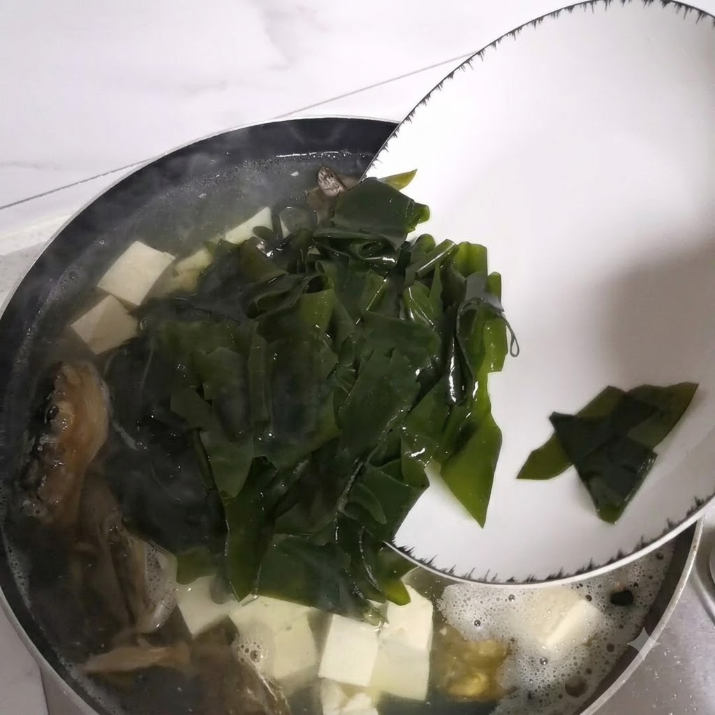 접시에 담긴 불린 미역을 끓고 있는 국 냄비에 넣는 모습.