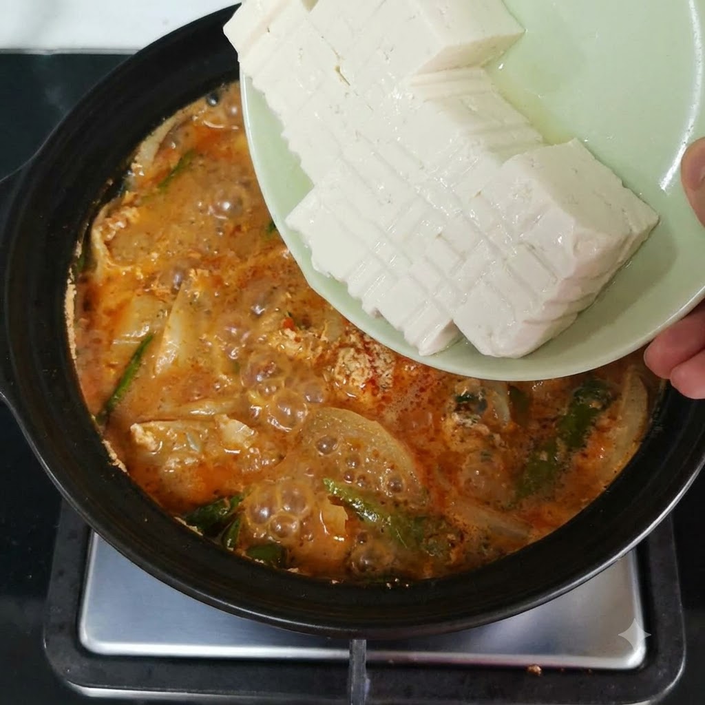 썰어둔 순두부를 붉은 국물과 채소가 담긴 끓는 뚝배기에 조심스럽게 넣는 모습.