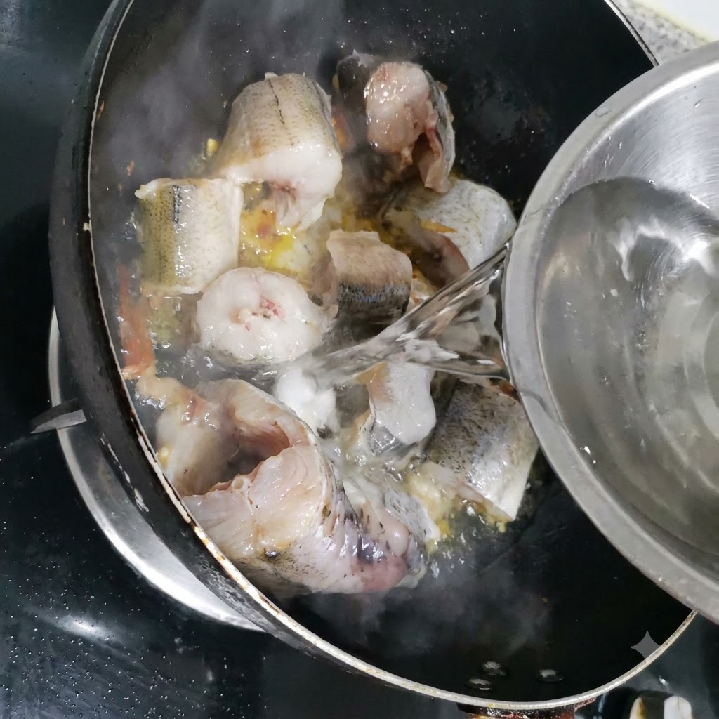 금속 볼에 담긴 물이 명태 조각들이 있는 팬 안으로 부어지고 있는 모습.