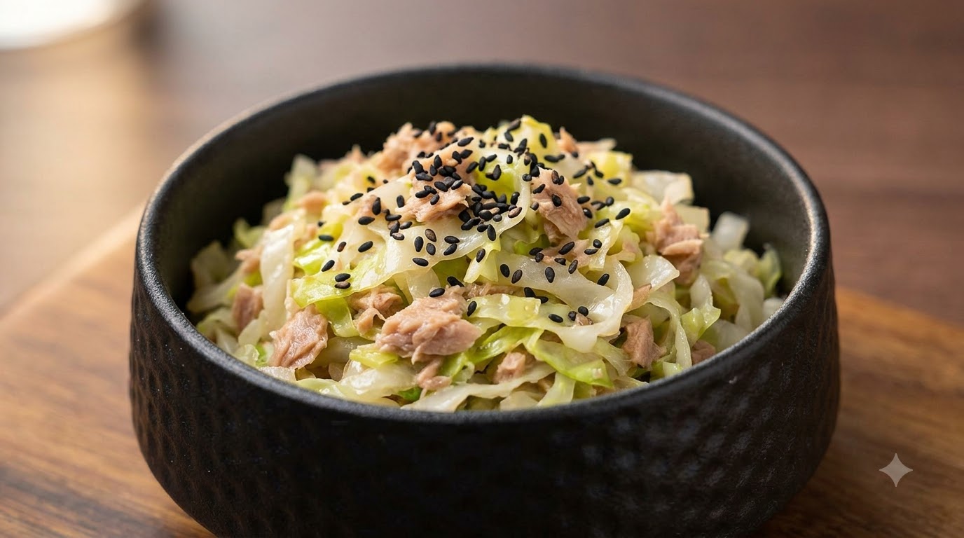 검은 참깨로 장식된 감칠맛 나는 참치 양배추 볶음이 담긴 작은 검은색 그릇
