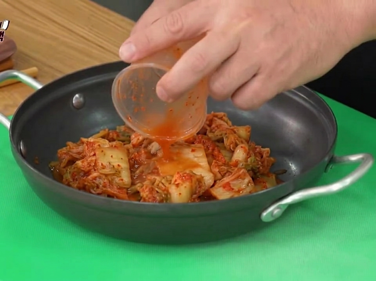 플라스틱 용기에 담긴 신김치가 검은색 조리용 냄비에 옮겨 담기는 모습.