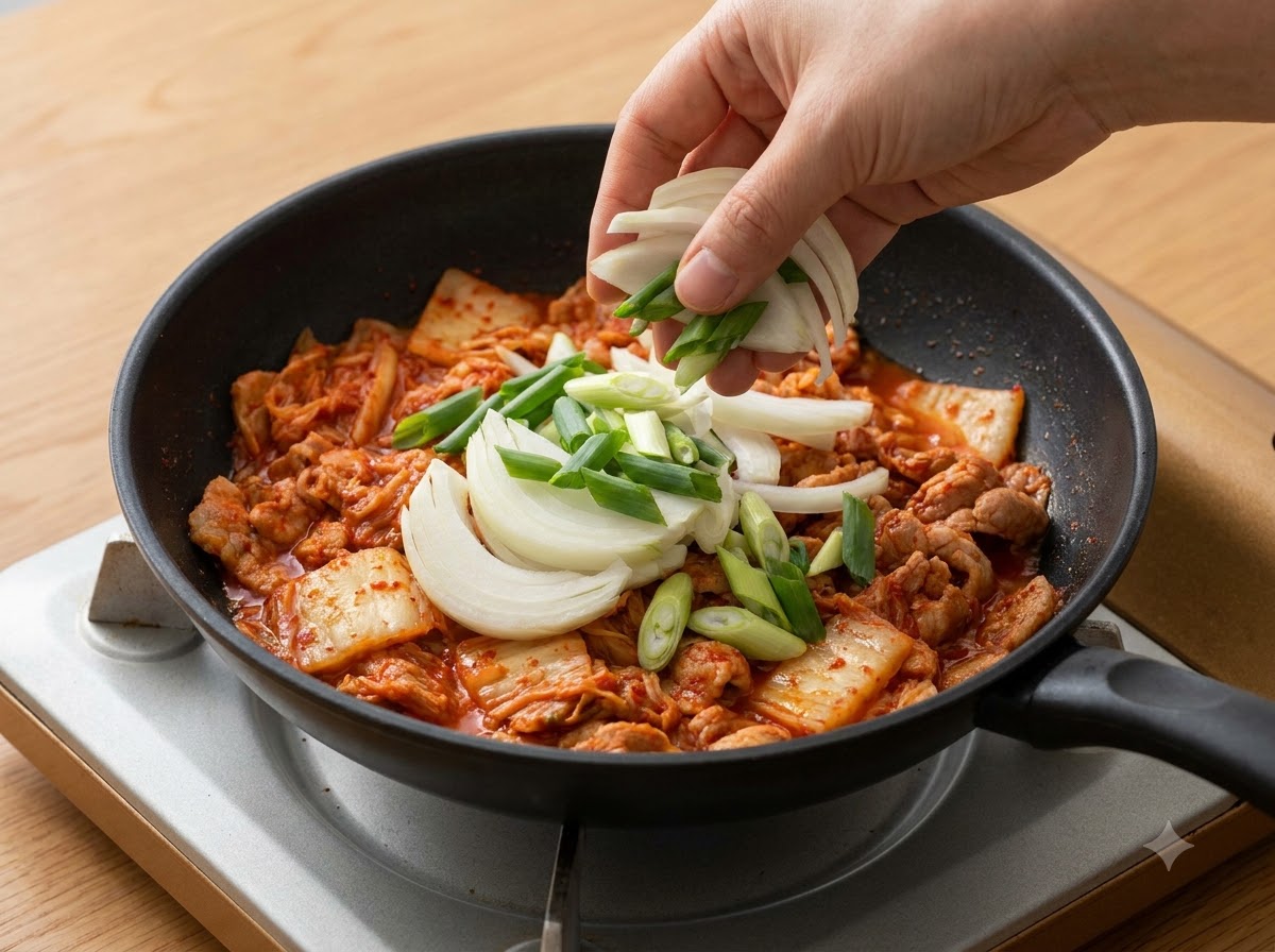 썰어둔 양파와 대파가 냄비 속 김치 위로 더해지는 모습.