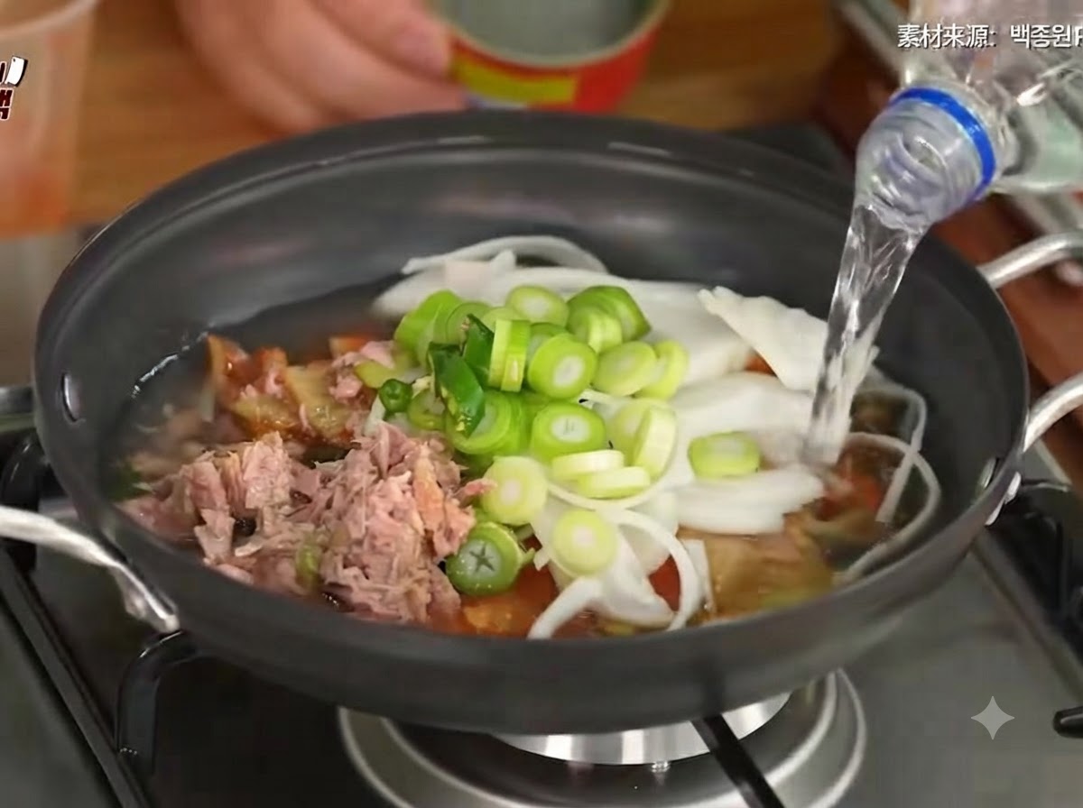 김치, 채소, 참치가 담긴 냄비에 물이 부어지고 있는 모습.