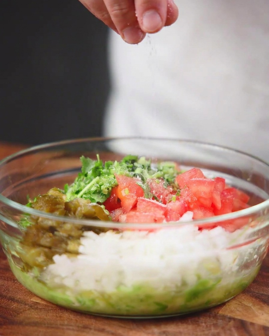 다진 토마토, 양파, 고추, 허브가 가득 찬 투명 유리 볼 위로 바다 소금이 위에서 솔솔 뿌려지는 모습.