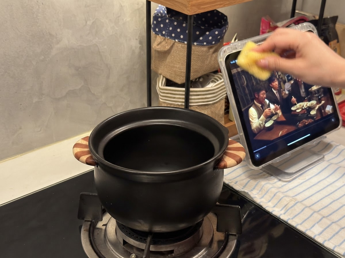 가스 렌지 버너 위에 놓인 작은 검은색 도자기 냄비.