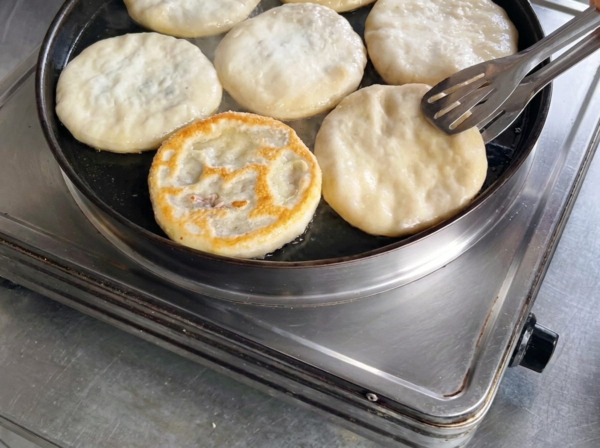 프라이팬에서 금속 집게를 이용해 고기파이를 뒤집어 노릇하고 바삭해진 윗면을 드러내는 모습.