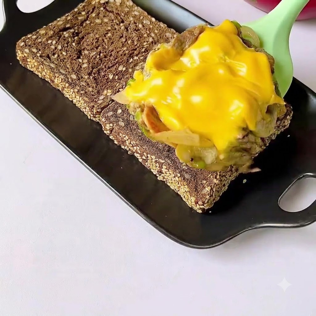 검은색 접시에 놓인 구운 통밀빵 위에 조리된 소고기와 녹은 치즈 혼합물이 숟가락으로 얹어지고 있는 모습.