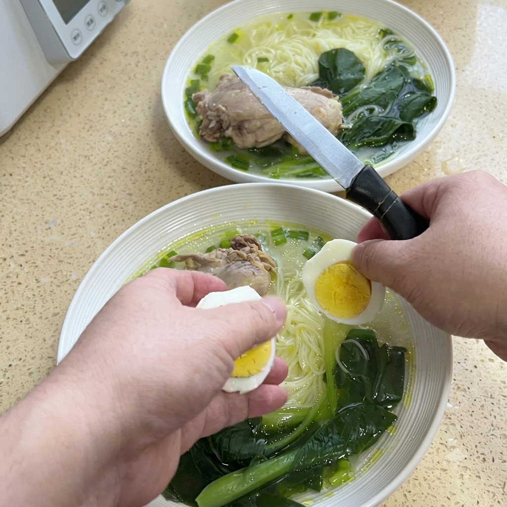 국수 그릇 위에서 칼로 완숙 달걀을 반으로 자르고 있는 두 손.