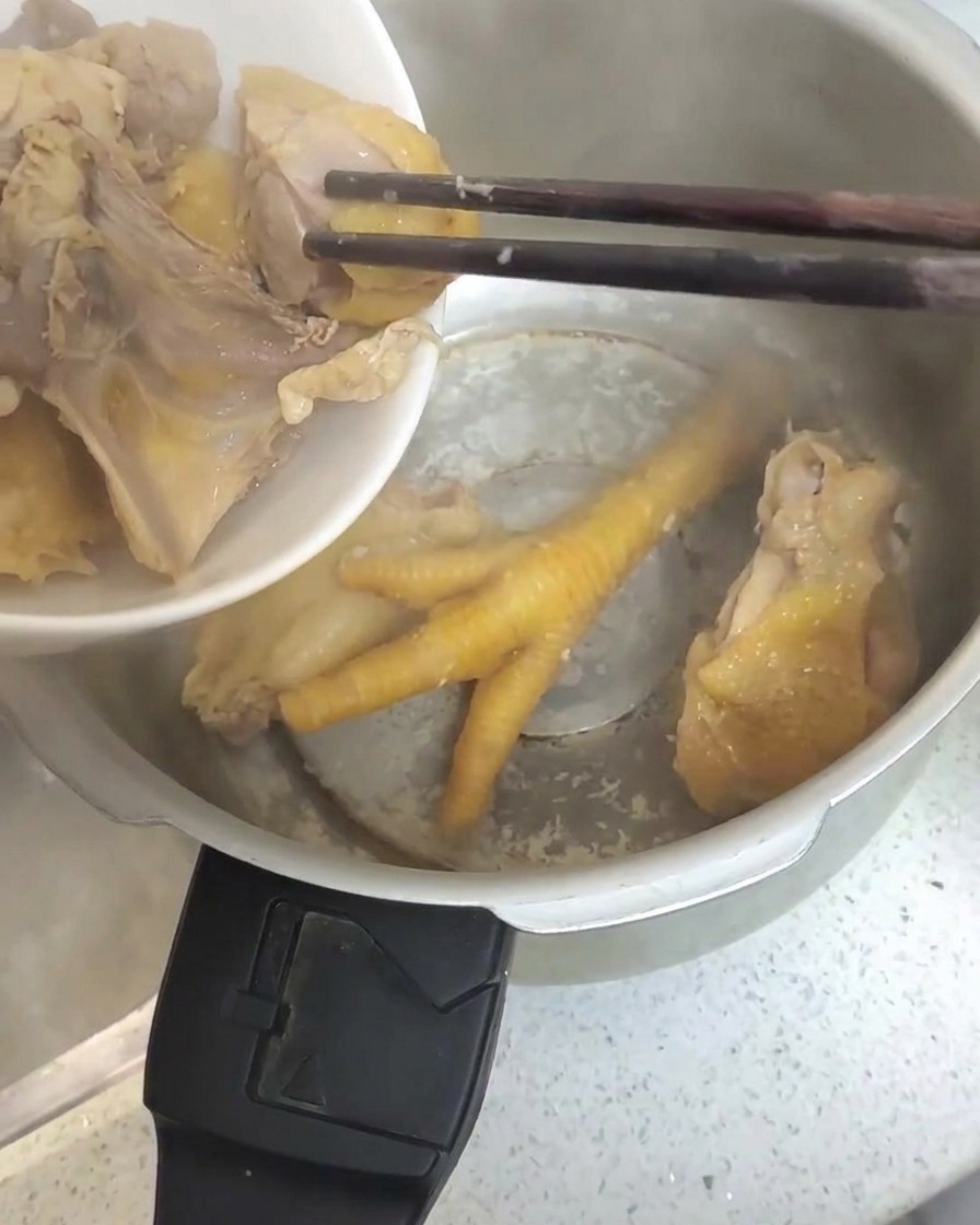 잘 데쳐진 닭고기 조각들이 젓가락으로 집혀 스테인리스 압력솥으로 옮겨지는 모습.