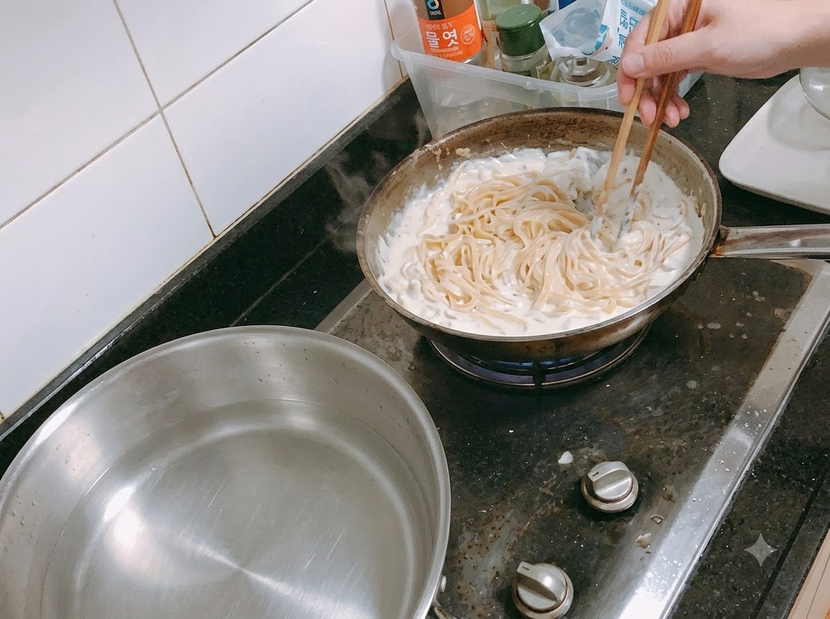 젓가락을 이용해 끓고 있는 크림소스에 파스타를 섞는 모습.