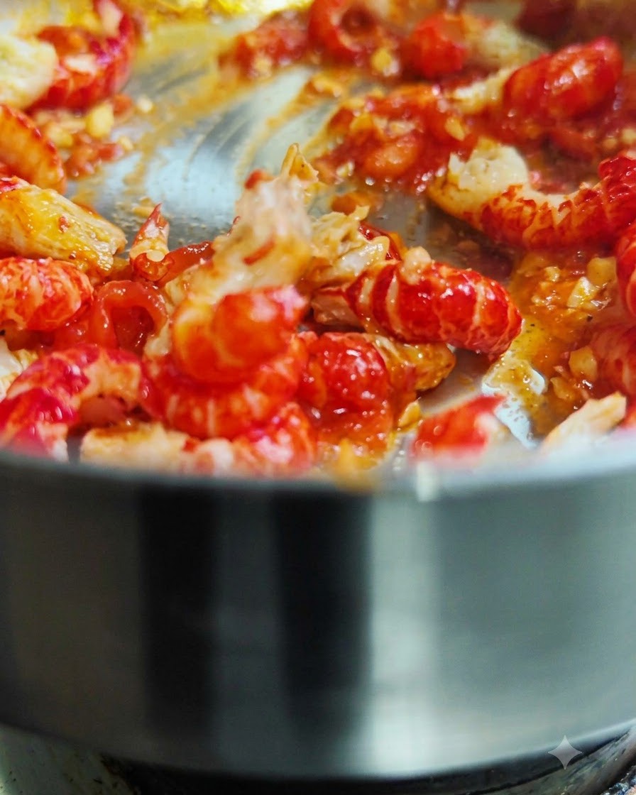 붉은 토마토 소스가 담긴 뜨거운 팬에서 껍질 깐 크롤피쉬를 함께 볶고 있는 모습.