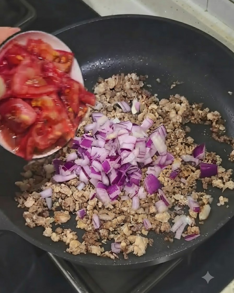 작은 그릇에 담긴 신선한 다진 토마토가 고기와 양파가 있는 팬에 추가되는 모습.