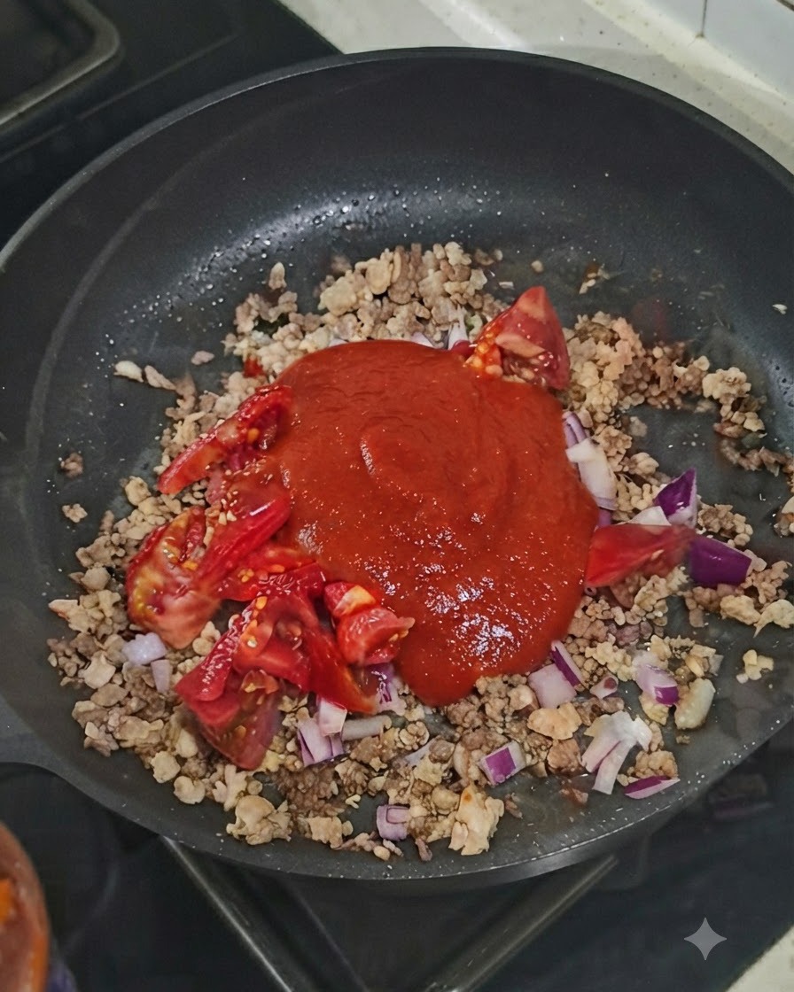 팬 안의 재료 위에 한 숟가락의 토마토 페이스트가 얹혀 있는 모습.
