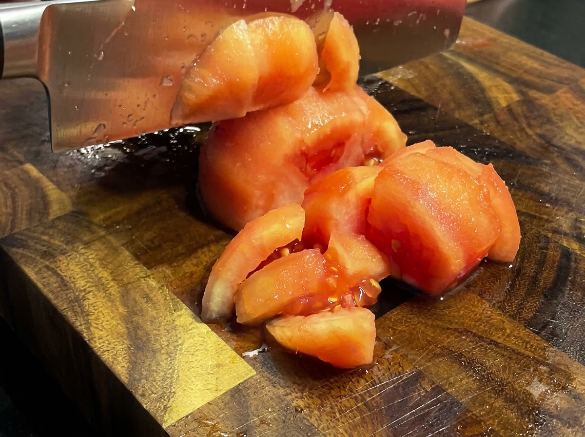 나무 도마 위에서 껍질을 벗긴 구운 토마토를 식칼로 깍둑썰기하는 모습.